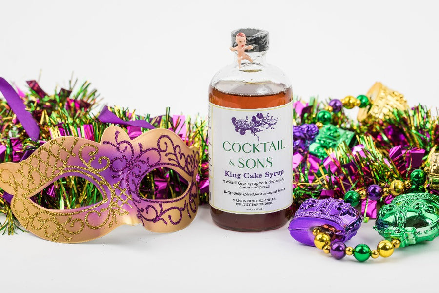 Cocktail and Son's King Cake syrup surrounded by Mardi Gras masks and beads 